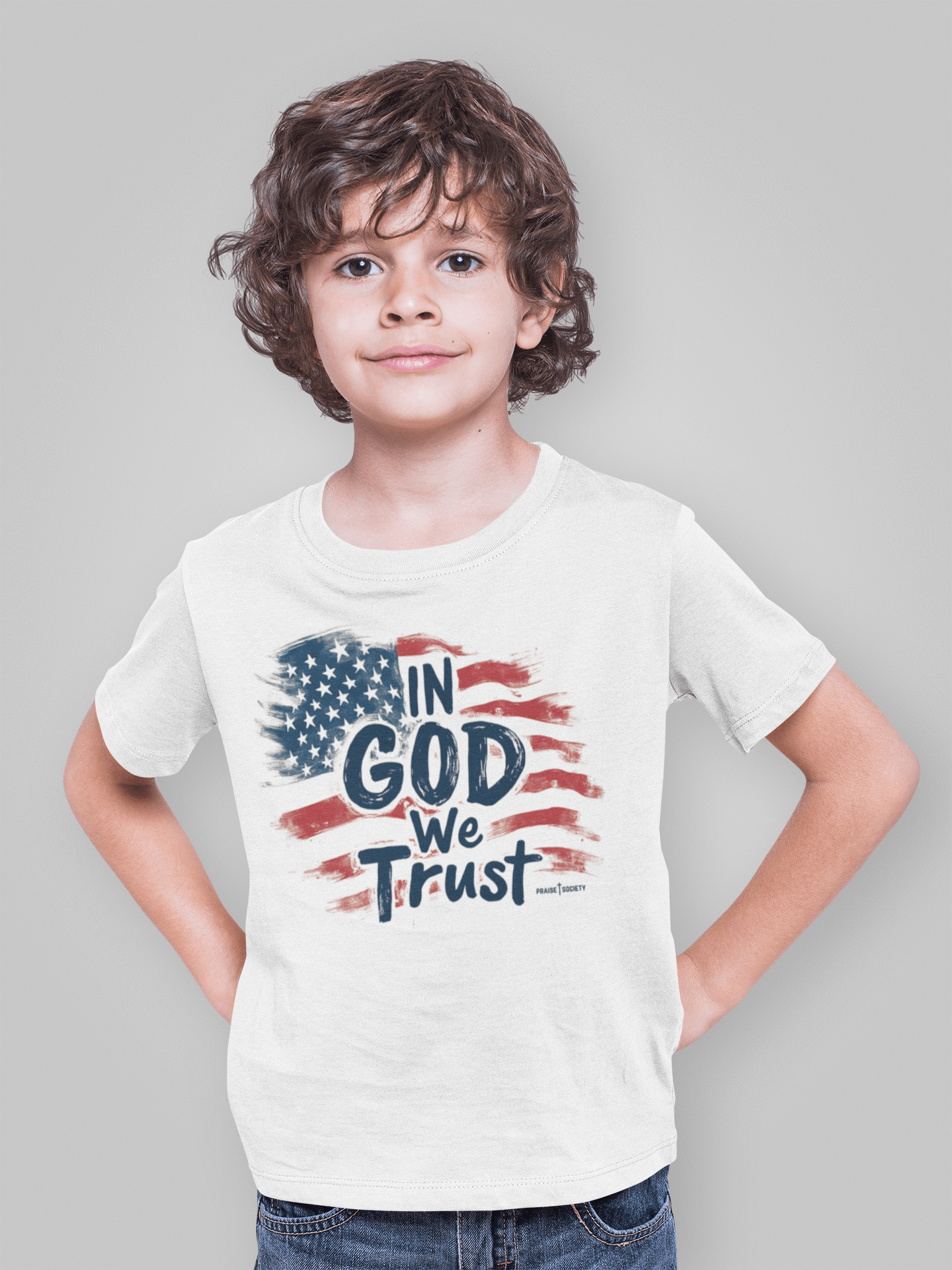 little boy wearing a white tshirt with text in God we trust on it by Praise Society Kids