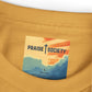 Close-up of a mustard yellow garment with a 'Praise Society' label featuring a colorful design.