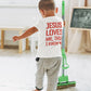 Child wearing a shirt with 'Jesus loves me, this I know' while holding a mop.