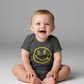 Baby sitting on a plain background wearing a dark gray onesie with a smiley face design.