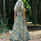 Woman wearing a floral dress standing in a natural setting with greenery.