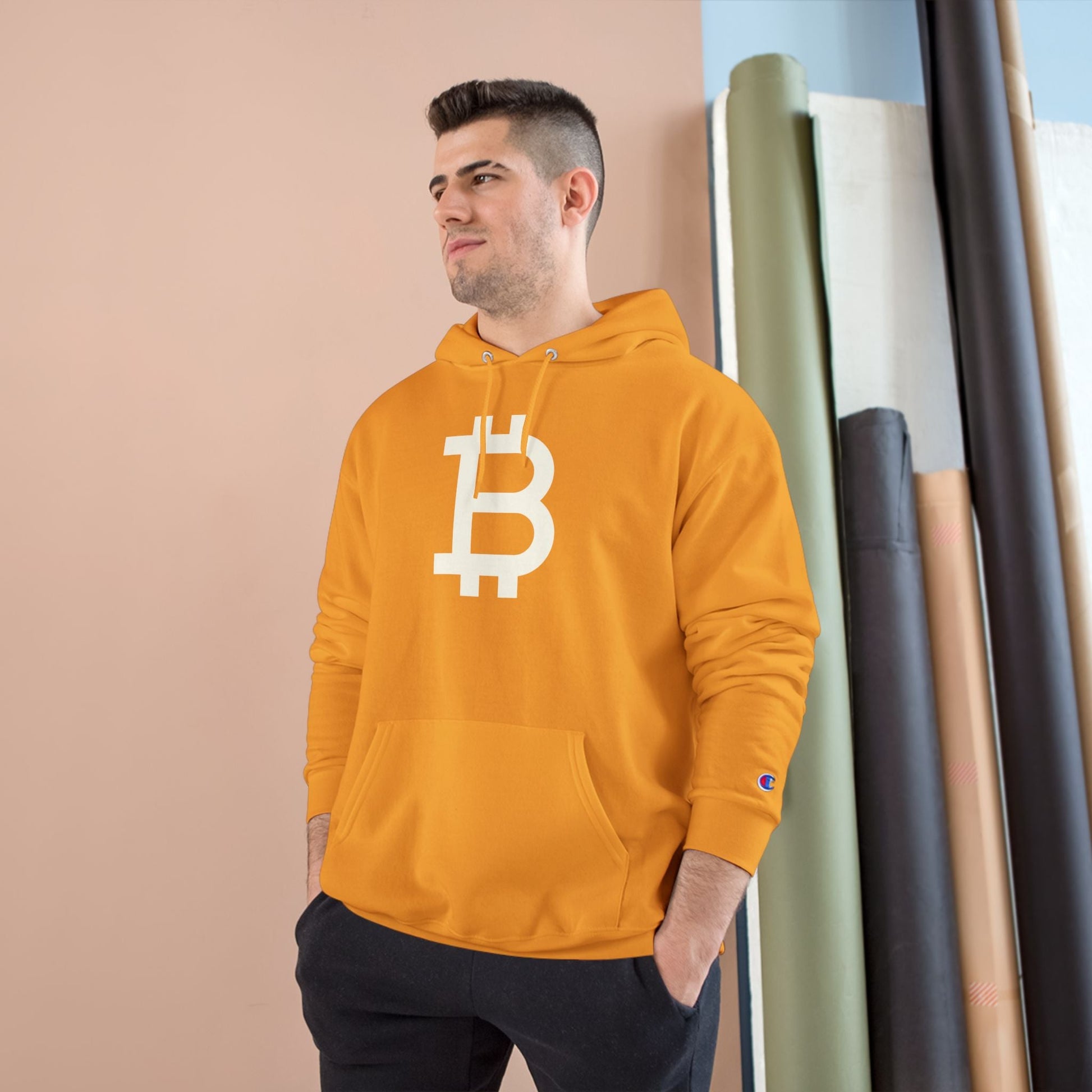 Man wearing a (Gold) hoodie with a Bitcoin logo against a neutral background