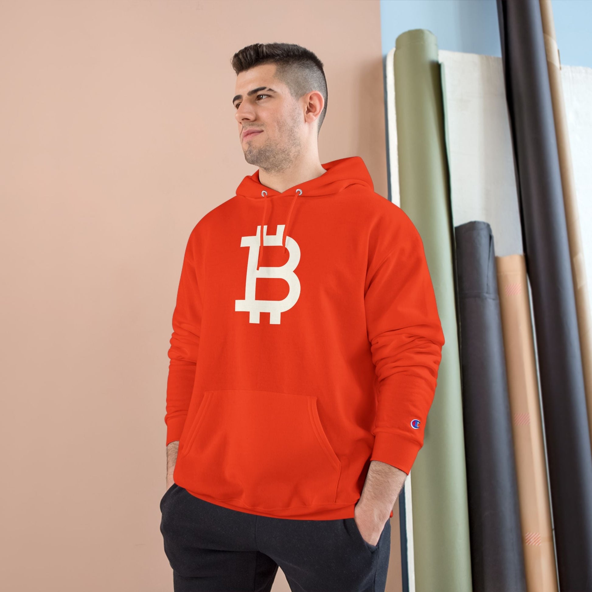 Man wearing a (Orange) Bitcoin hoodie with a Bitcoin logo against a beige wall.