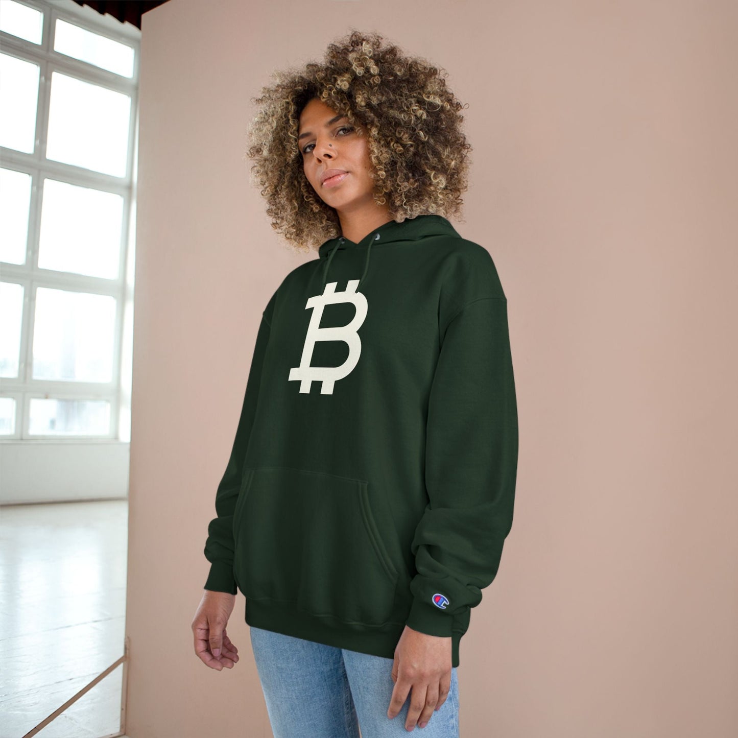 Person wearing a (Dark Green) hoodie with a Bitcoin logo against a beige wall.