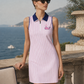 Woman wearing a pink dress with a blue collar and whale logo, standing by a scenic ocean view.