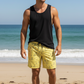 Man wearing a black tank top and yellow bitcoin swim shorts on a beach