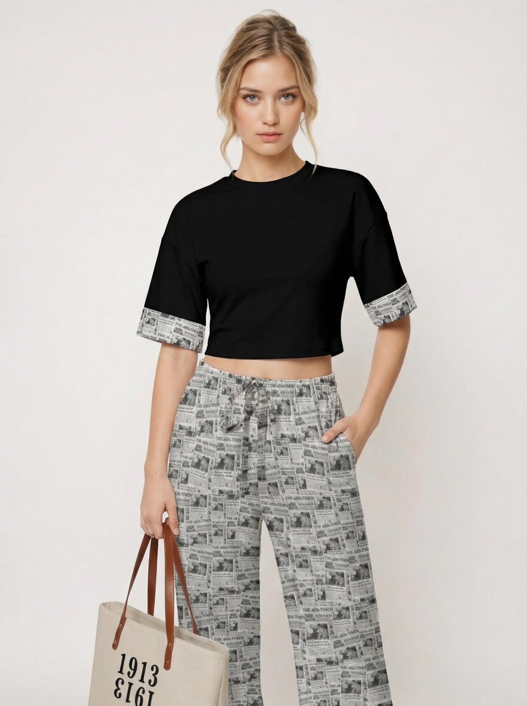 Woman wearing a black top and patterned pants, holding a tote bag with text.