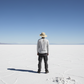 Person standing on a vast, flat salt flat with a clear blue sky.