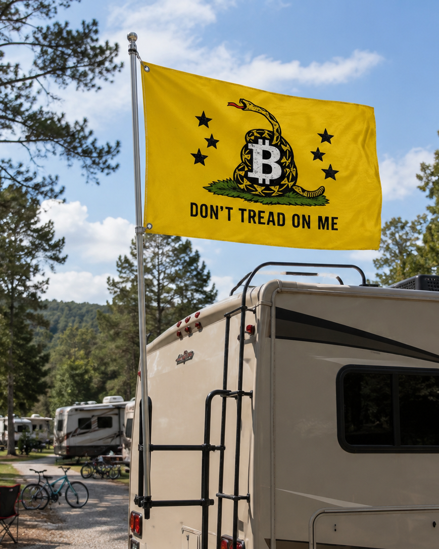 A yellow Gadsden-style flag with a coiled snake, black stars, a large B, and the text 'DON'T TREAD ON ME' mounted on a pole in front of an RV at a campsite.