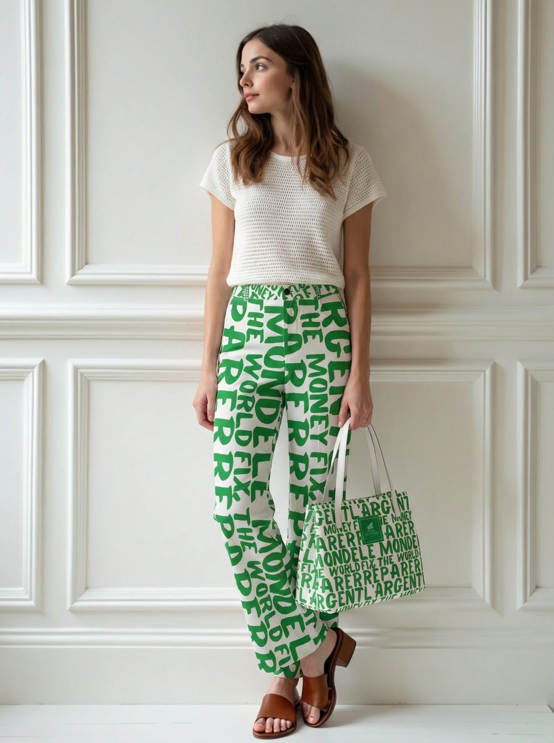 Woman wearing green patterned fix the money fix the world Bitcoin pants and holding a matching bag against a white paneled wall.