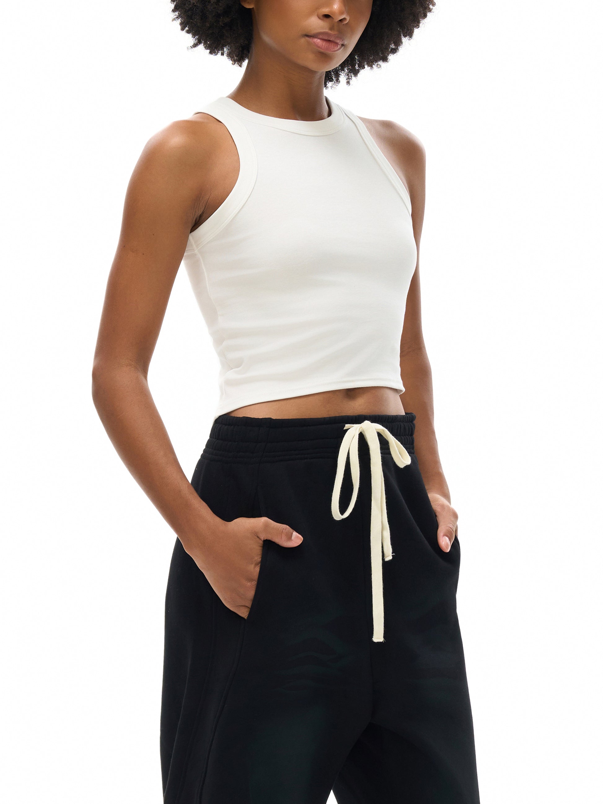 Person wearing a white sleeveless top and black pants with a drawstring on a white background