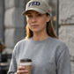 Model holding coffee outside a cafe in the Sandstone Not A FED Sunwashed Cap with navy embroidery and red side script.