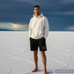 Man wearing satoshi smiles black shorts standing on a salt flat with a dark sky and mountains in the background - SVRN Society