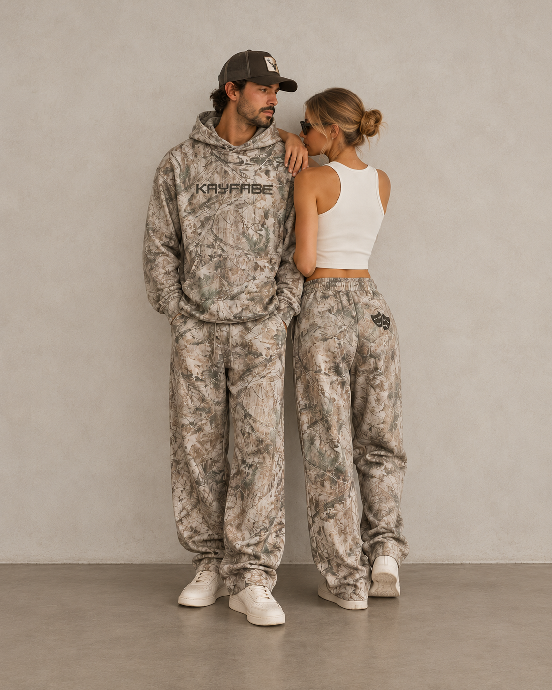 Man and woman wearing Kayfabe tree camo fleece sweatpants, man also in matching hoodie
