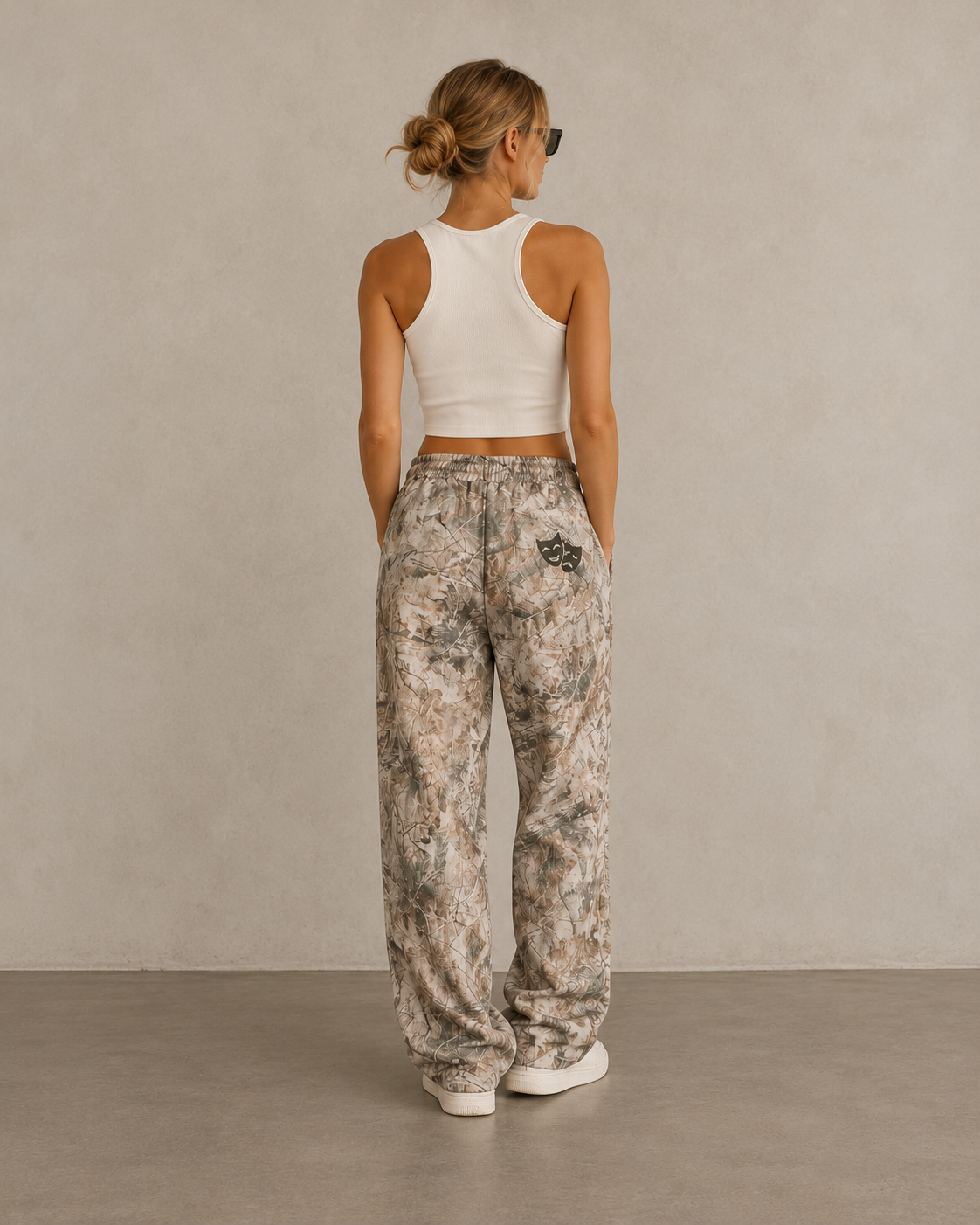 Woman in white tank top wearing Kayfabe tree camo fleece sweatpants, back view