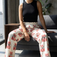 Woman wearing a black sleeveless top and tax the rich pants with red text, sitting on a couch - svrn society.
