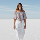 Woman in a nautical off-shoulder top and white pants standing on a salt flat with blue sky.