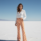 Woman wearing a white shirt and orange patterned bitcoin b pants standing on a salt flat with blue sky.
